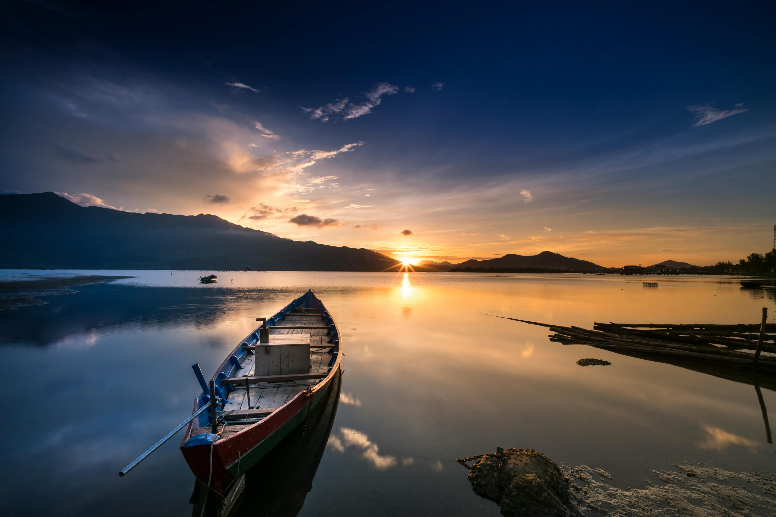 Tranquil sunset view with a boat on a calm lake reflecting mountains and golden sky.