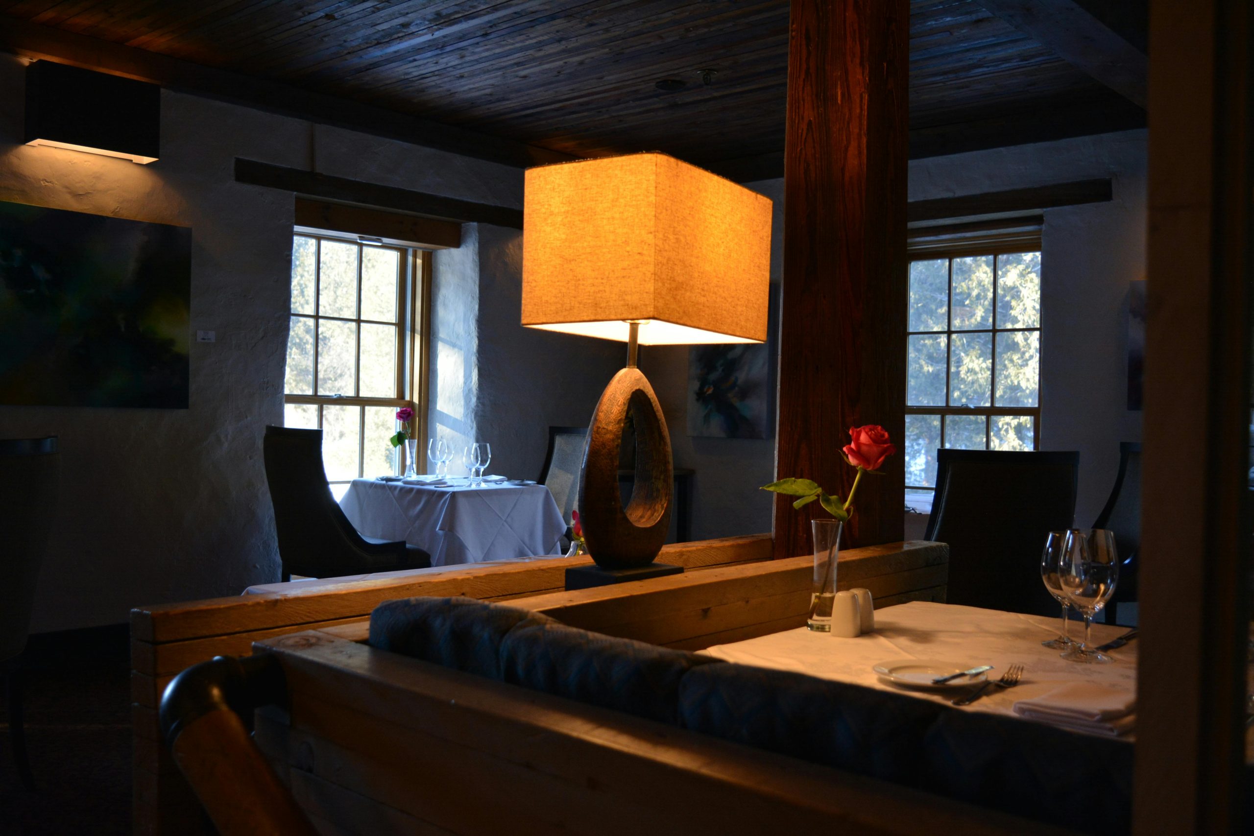 An elegant dining room featuring ambient lighting, a wooden interior, and a single rose centerpiece on the table.