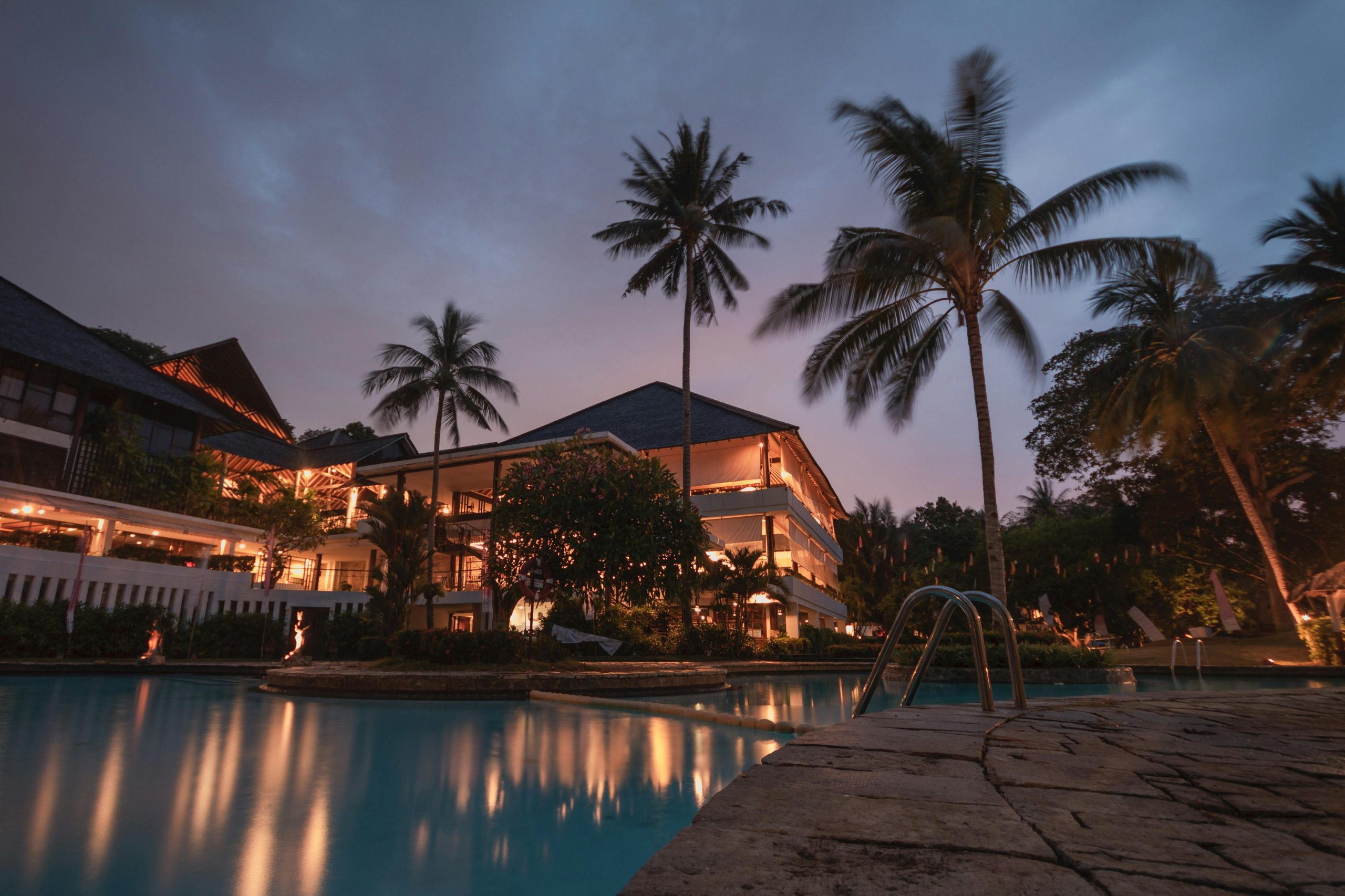 Luxurious tropical resort with swimming pool and palms at dusk, perfect for a tranquil vacation.